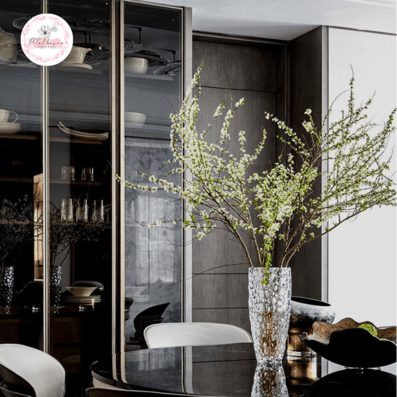 Bàn tay đang sắp xếp các cành hoa tuyết mai trắng vào một chiếc bình thủy tinh, thể hiện kỹ thuật cắm hoa tạo dáng tự nhiên.
