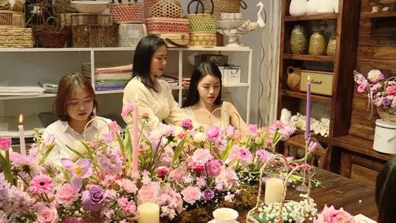 Một nhóm người đang cùng nhau cắm hoa và trò chuyện vui vẻ trong một workshop về hoa, tượng trưng cho cộng đồng yêu hoa nơi chia sẻ đam mê và kiến thức