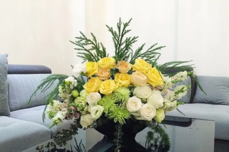 Một bình hoa lớn được cắm đẹp mắt đặt trên bàn ăn trong một căn phòng khách hiện đại, thể hiện ý nghĩa của hoa trong việc trang trí và nâng tầm không gian sống