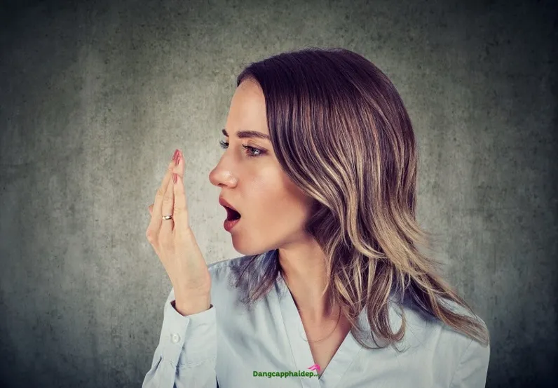Một phụ nữ dùng tay kiểm tra hơi thở, minh họa việc nhận biết mùi cơ thể ảnh hưởng đến giao tiếp.