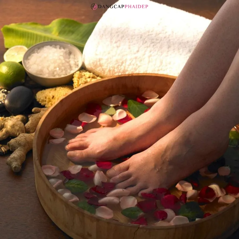 Một phụ nữ ngâm chân trong chậu nước ấm với cánh hoa, giúp thư giãn và khử mùi hôi chân hiệu quả.