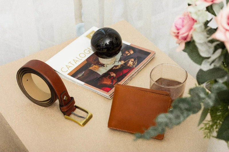 Chiếc ví da màu nâu và đồng hồ đeo tay trên bàn gỗ, cạnh ly cà phê